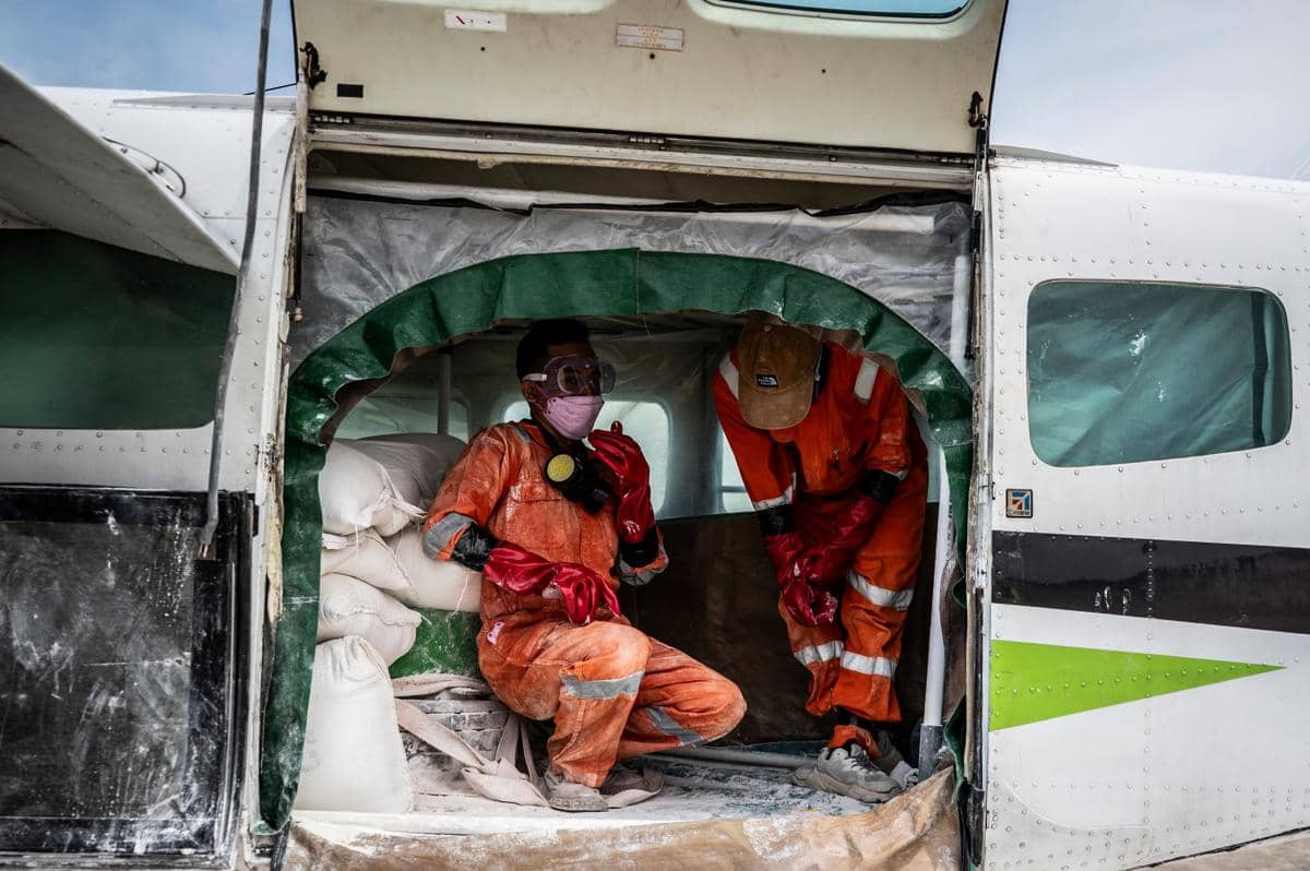 Dua petugas BNPB mengenakan pakaian pelindung oranye bersiap di dalam pesawat Cessna 208 Caravan untuk Operasi Modifikasi Cuaca di Semarang.