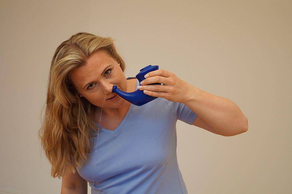 Seorang perempuan membersihkan hidung dengan metode iritasi nasal menggunakan neti pot.