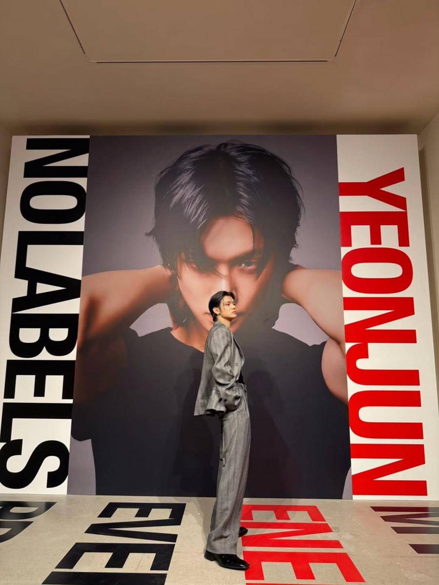 Yeonjun TXT berpose dengan latar belakang poster besar "NO LABELS"