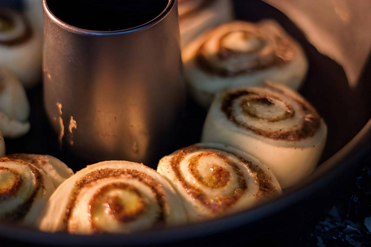 Beberapa adonan cinnamon roll sedang dipanggang dalam loyang bundt, memperlihatkan lapisan kayu manis yang mulai kecokelatan.