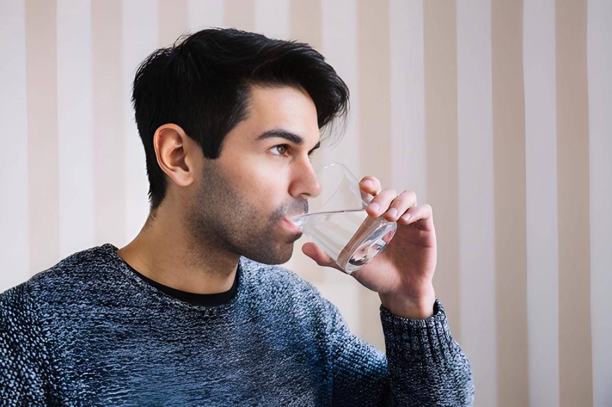 Seorang laki-laki minum segelas air putih.