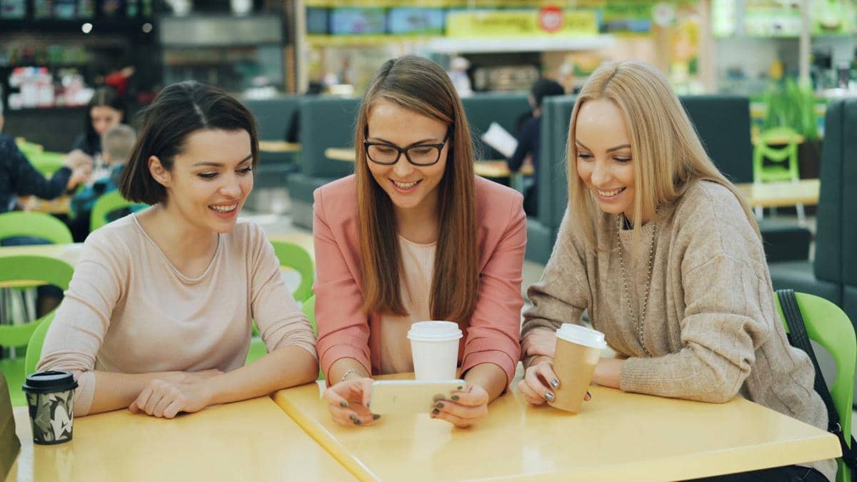 Sekelompok grup pertemanan berisi 3 orang wanita muda sedang memperhatikan layar smartphone.