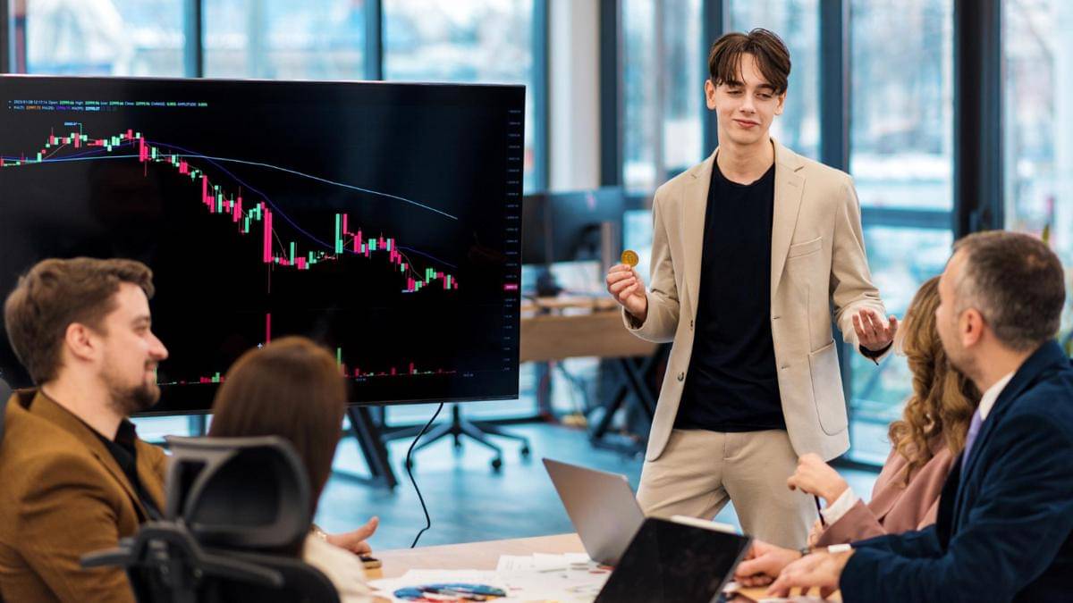sekelompok orang sedang memutuskan rencana investasi dengan layar monitor besar yang menampilkan candlestick saham.