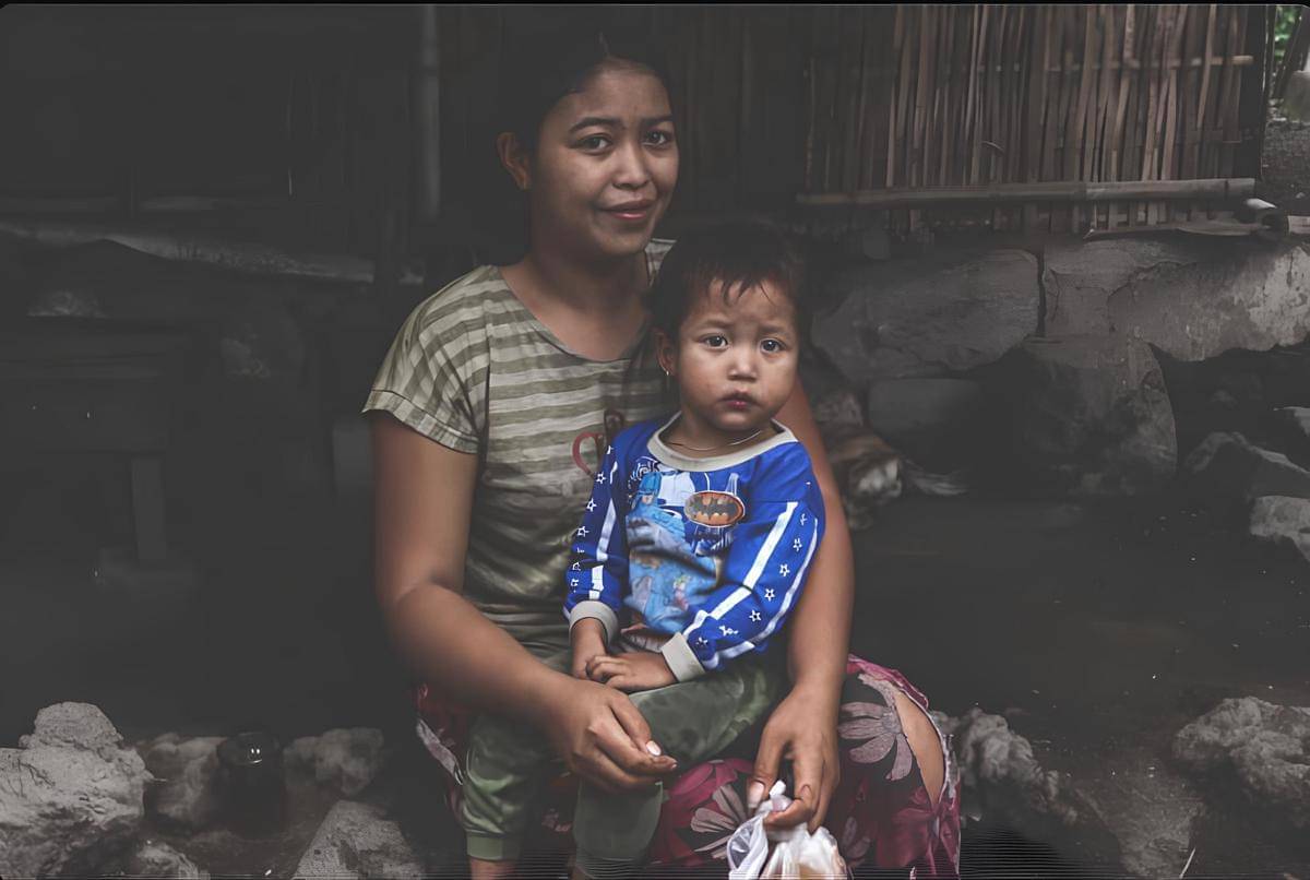 Seorang ibu, yang sedang menggendong anak, tampak tersenyum karena tersedianya akses air bersih yang lebih mudah berkat program Sumber Air untuk Sesama (SAUS).