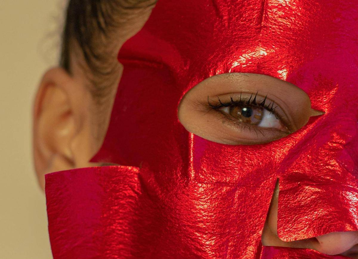 Seorang perempuan menggunakan sheet mask berwarna merah.