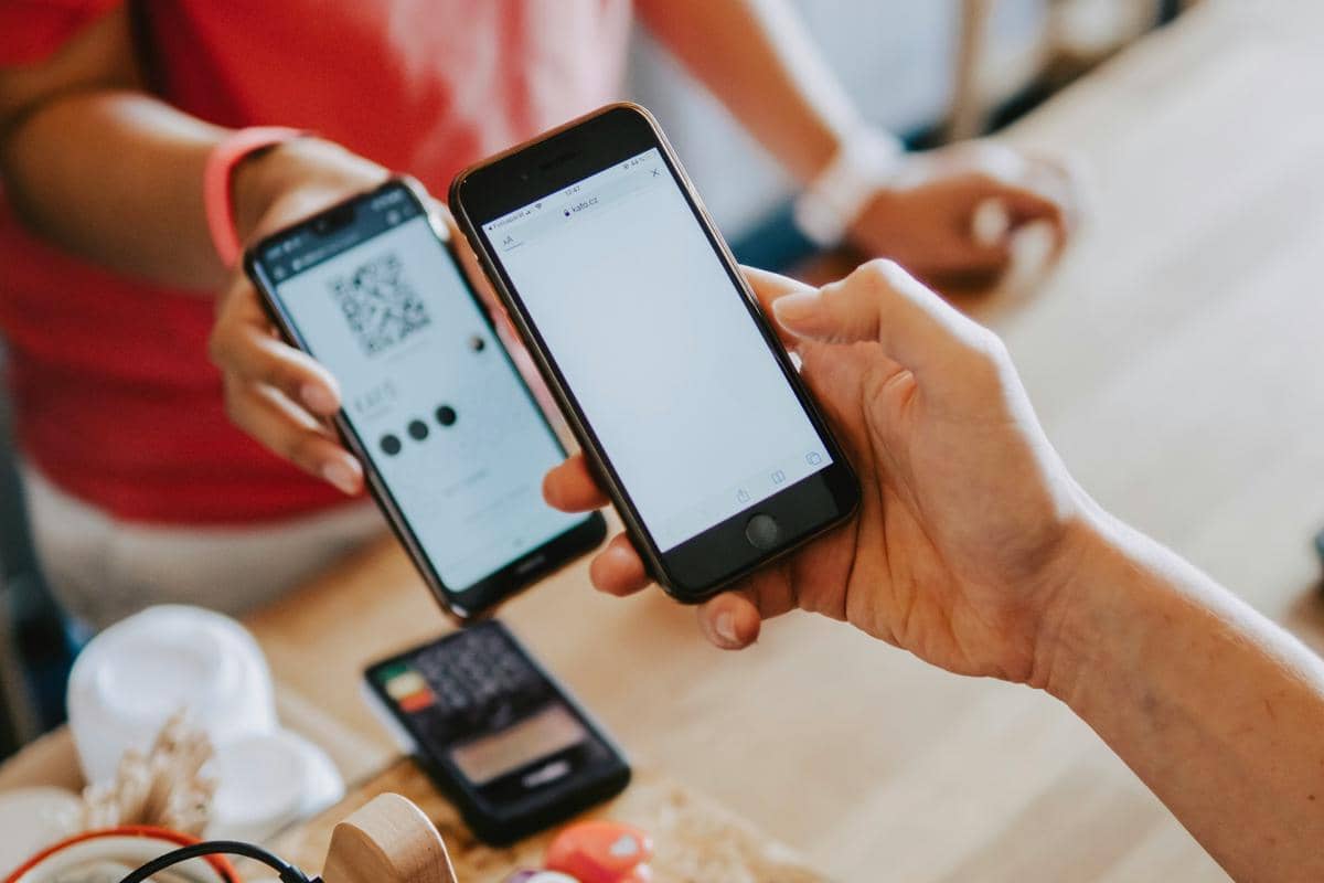 Ilustrasi dua orang sedang melakukan pembayaran digital dengan memindai kode QR menggunakan smartphone.