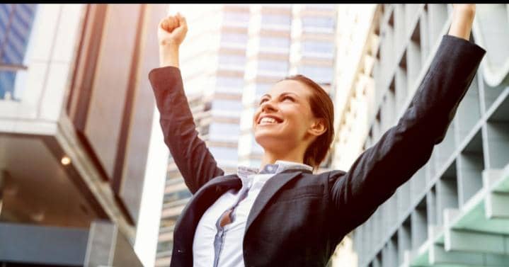 Perempuan bisnis tersenyum dengan tangan terangkat tinggi menunjukkan rasa kemenangan