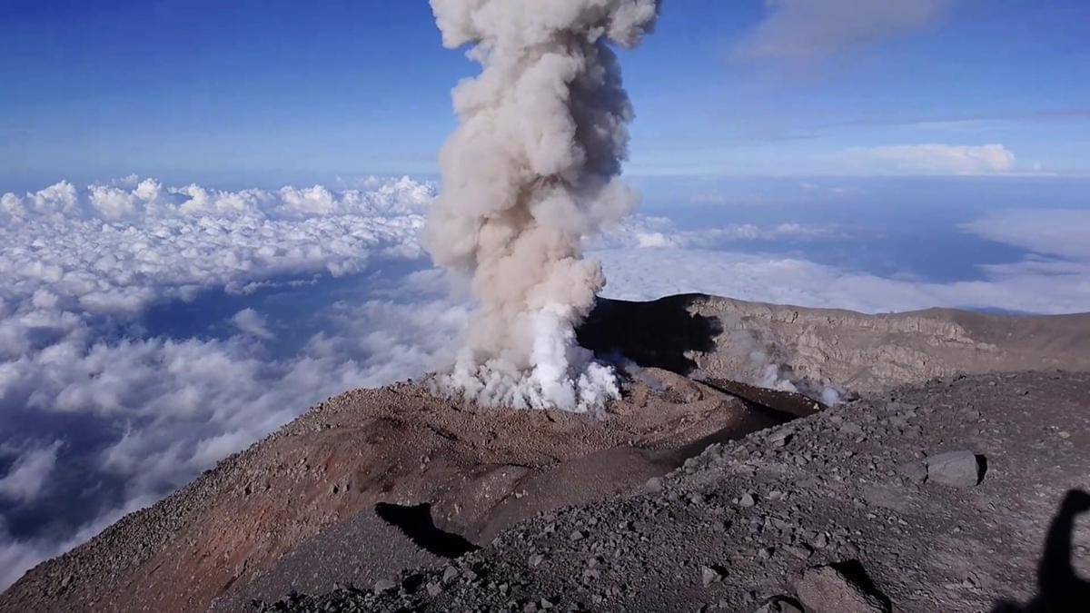 Pemandangan dekat kawah Semeru dengan semburan asap besar ke udara di atas lautan awan.