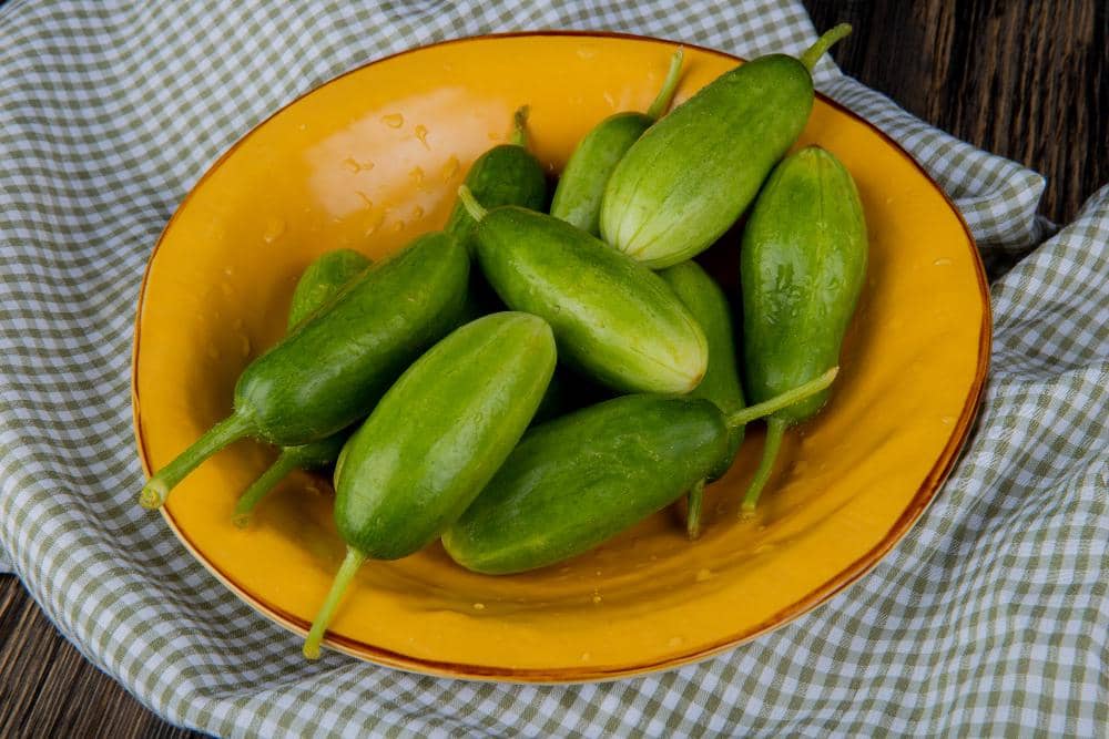Beberapa buah belimbing wuluh hijau segar di atas piring kuning yang diletakkan di atas kain bermotif kotak-kotak.