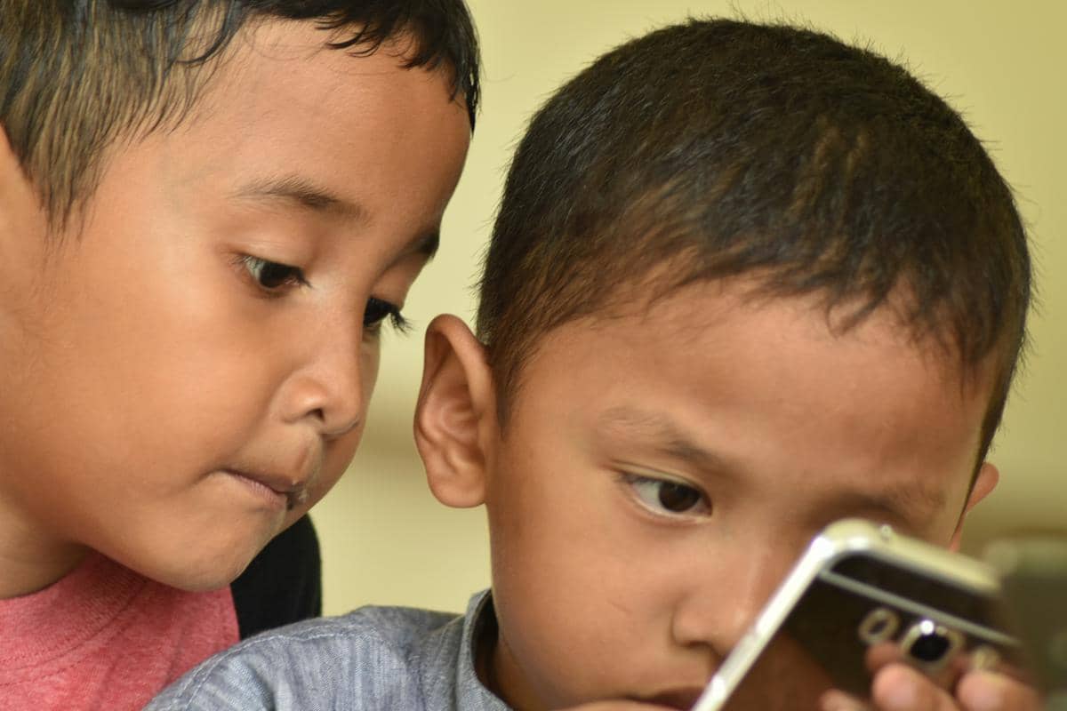 Dua anak menggunakan smartphone bersama dari jarak dekat.
