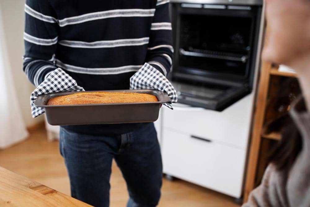 Ilustrasi seorang perempuan bersarung tangan oven mengeluarkan loyang berisi kue panggang dari oven di dapur.