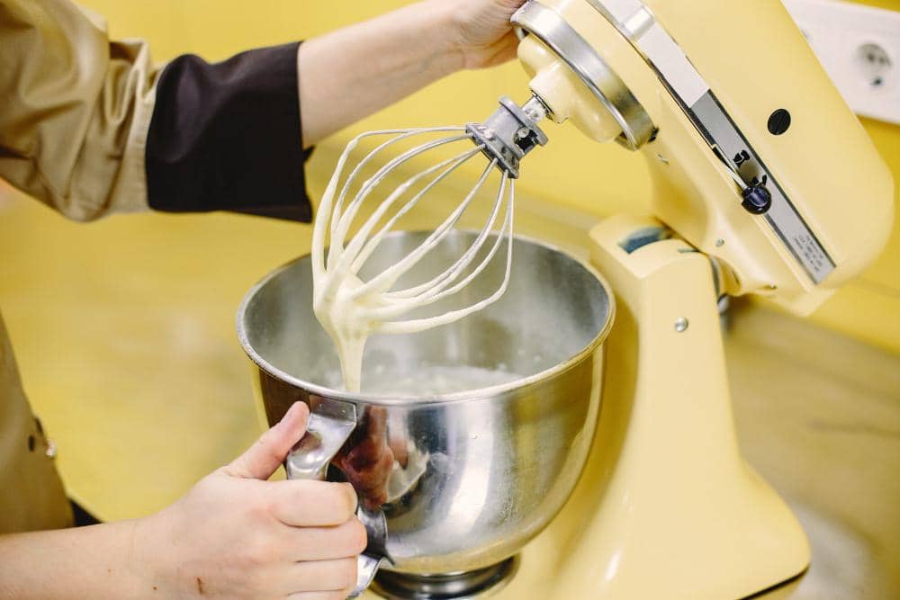 Ilustrasi penggunaan mixer listrik untuk mengaduk adonan kue di dalam mangkuk sebagai bagian dari proses memasak.