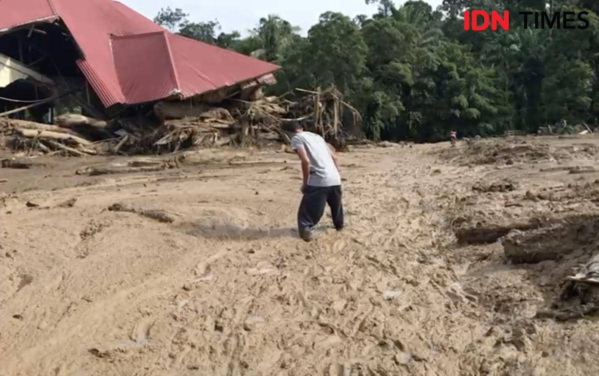 Seorang warga melintasi endapan lumpur usai banjir bandang untuk membantu proses evakuasi di Palembang, Kabupaten Agam. (IDN Times/Halbert Caniago)