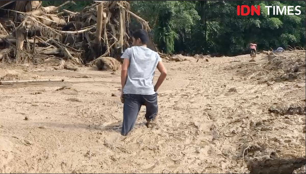 Seorang warga melintasi endapan lumpur usai banjir bandang untuk membantu proses evakuasi di Palembang, Kabupaten Agam.
