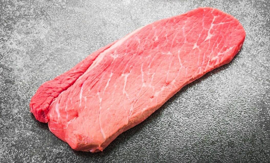 Potongan daging sandung lamur mentah berwarna merah muda dengan serat halus di atas permukaan meja batu abu-abu.