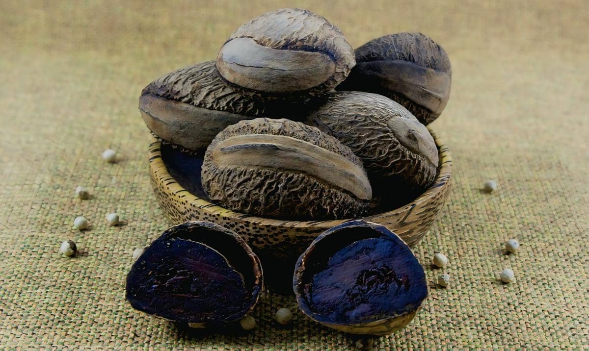 Beberapa biji kluwek berwarna cokelat tua dengan tekstur kasar dalam mangkuk kayu, sebagian dibelah memperlihatkan bagian dalam berwarna hitam pekat.