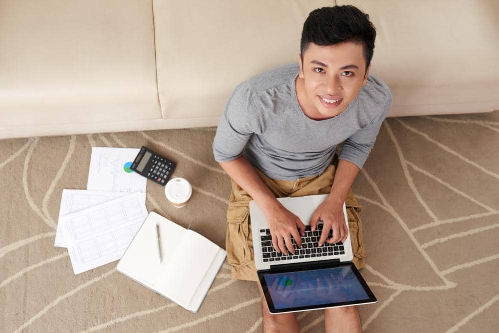Asian man working on laptop sitting on floor from above