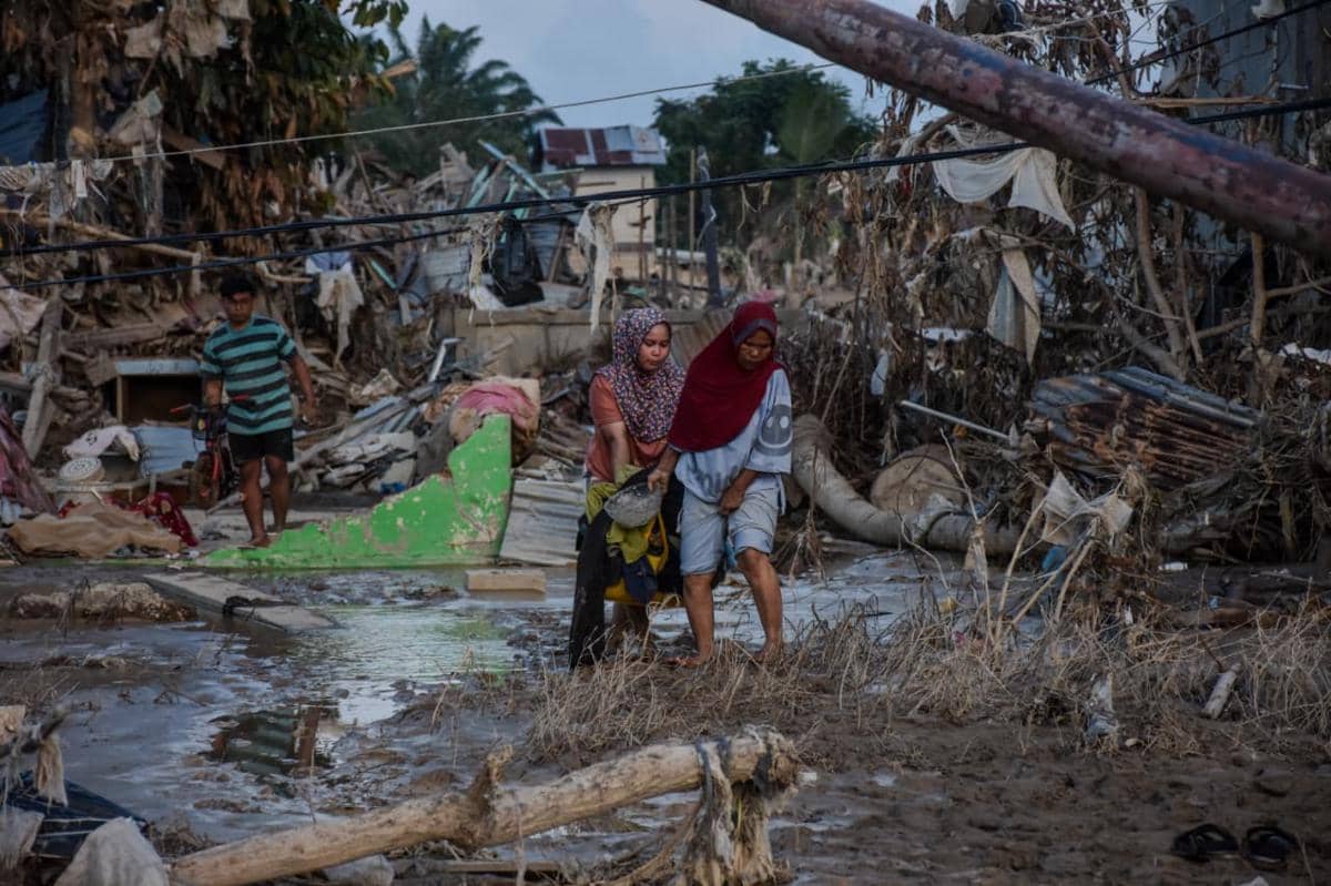 Warga Aceh Tamiang berjalan di tengah sisa puing-puing rumah, Jumat (5/12/2025) (IDN Times/Prayugo Utomo)
