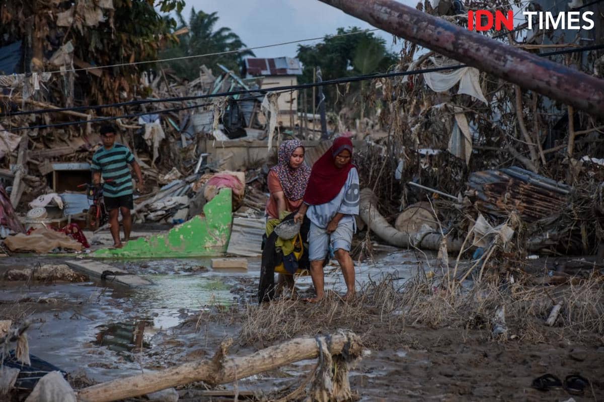Warga Aceh Tamiang berjalan di tengah sisa puing-puing rumah, Jumat (5/12/2025) (IDN Times/Prayugo Utomo)