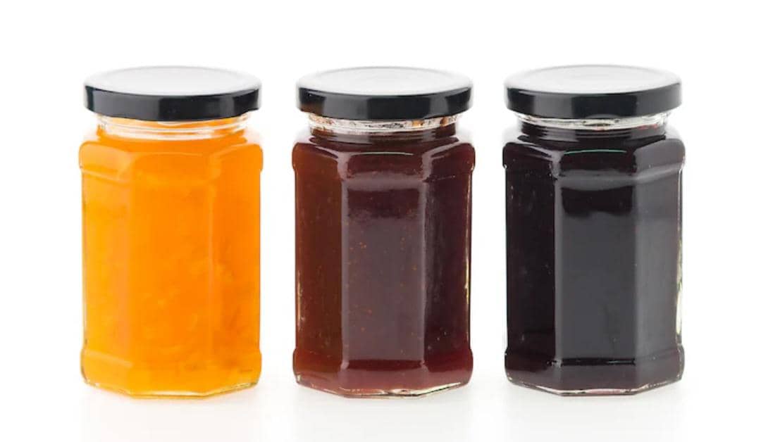 Tiga toples kaca berisi kecap dan saus berwarna oranye, cokelat, dan hitam dengan tutup hitam diletakkan berdampingan.