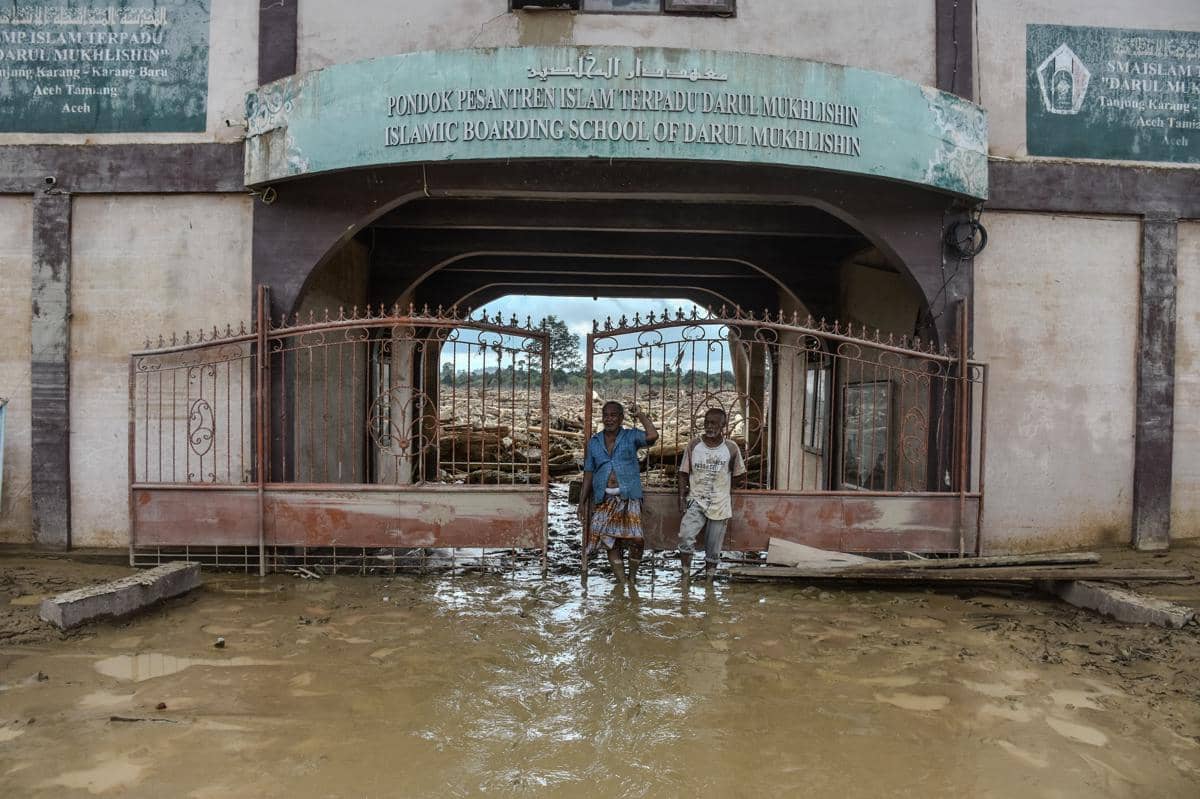 Dahnial (kiri) berdiri di depan gerbang Pesantren Darul Mukhlisin, Desa Tanjung Karang, Kecamatan Karang Baru, Aceh Tamiang, Sabtu (6/12/2025) (IDN Times/Prayugo Utomo)