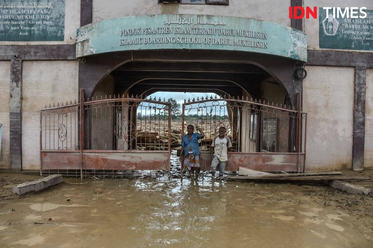 Dahnial (kiri) berdiri di depan gerbang Pesantren Darul Mukhlisin, Desa Tanjung Karang, Kecamatan Karang Baru, Aceh Tamiang, Sabtu (6/12/2025) (IDN Times/Prayugo Utomo)