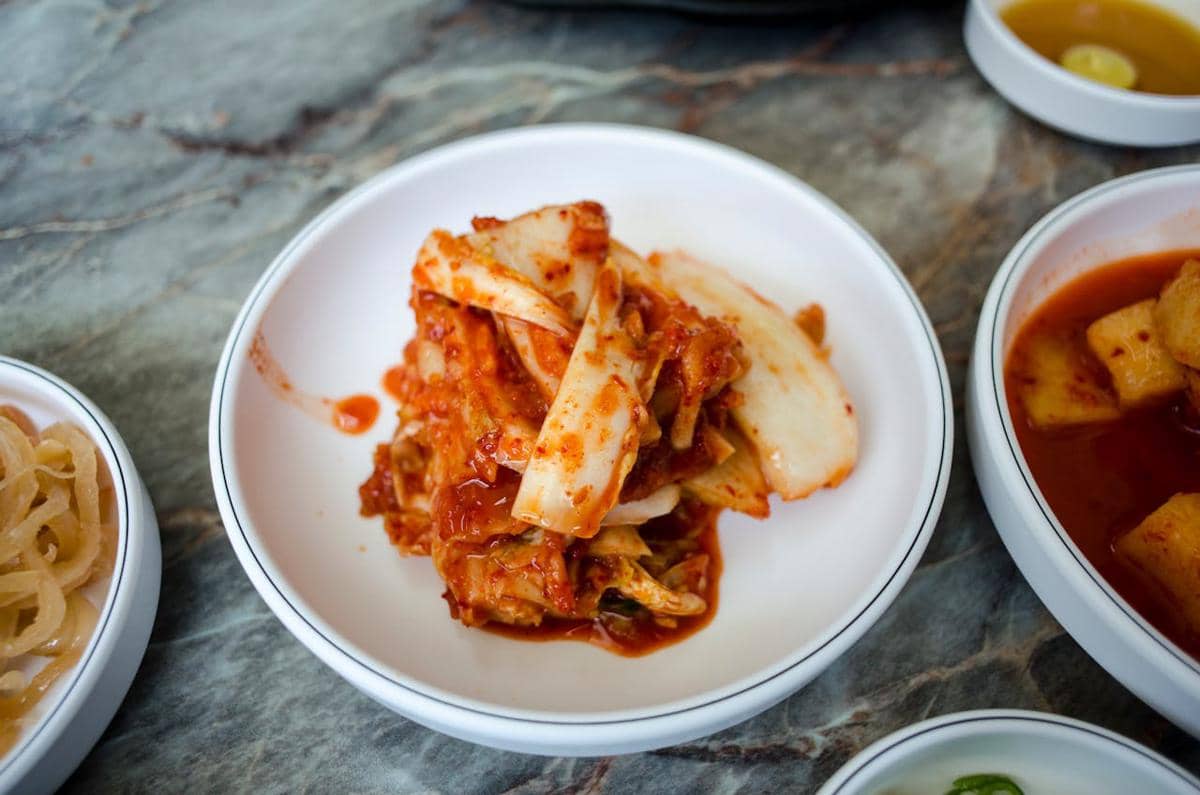 Ilustrasi kimchi, hidangan fermentasi khas Korea berupa sawi putih berbumbu merah dalam wadah saji.