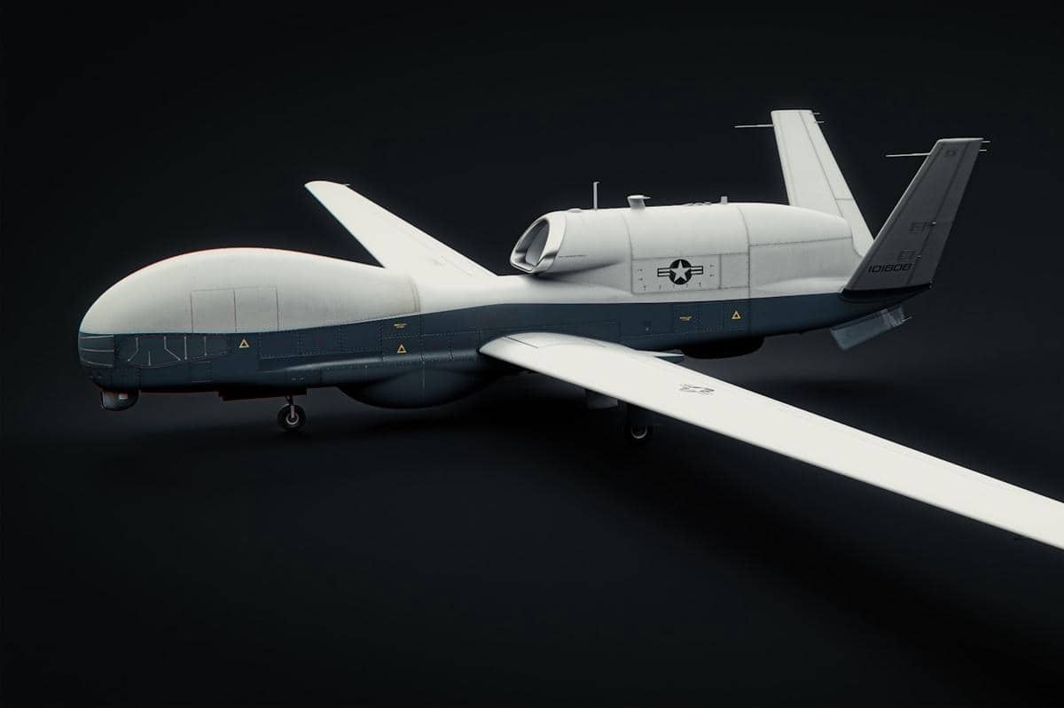 Drone militer tanpa awak berwarna abu-abu dan putih dengan desain aerodinamis serta lambang militer di badan pesawat.