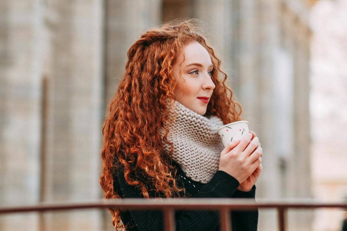 Wanita sedang tersenyum sambil membawa kopi hangat.
