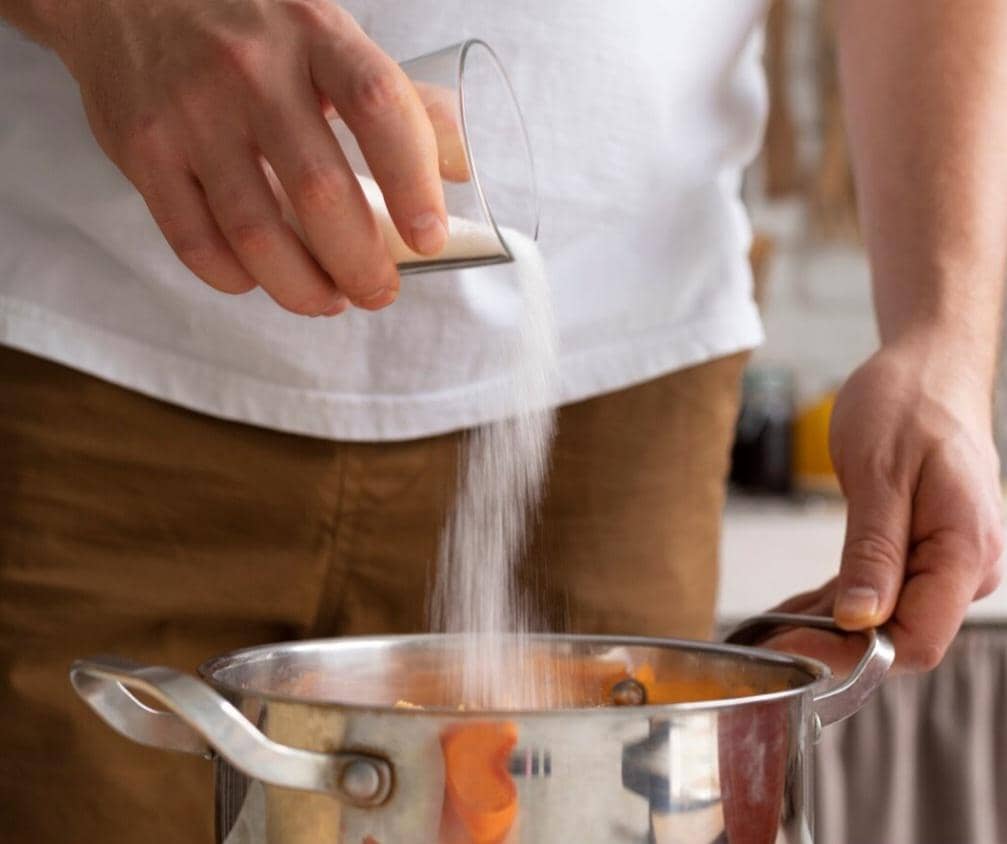 Seseorang menuangkan gula ke dalam masakan.