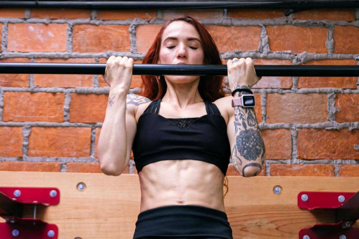 Seorang perempuan melakukan chin-up, perutnya sixpack.
