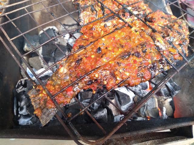 Ilustrasi ikan nila bakar berwarna kecokelatan disajikan di atas piring, tampak lezat dengan bumbu rempah.