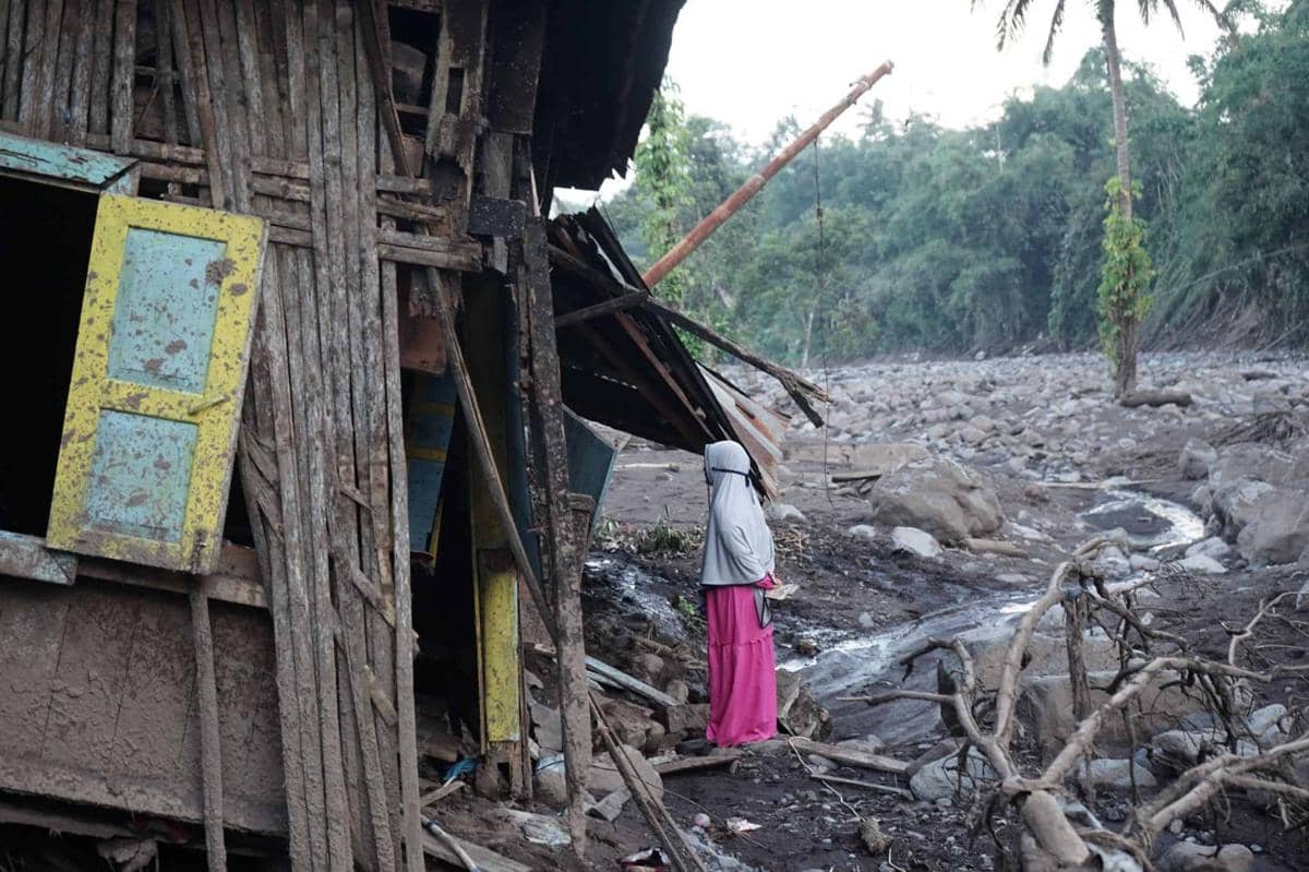 Seorang wanita berdiri di reruntuhan rumah akibat galado.