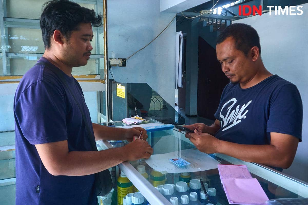 Juandika (kiri) menunjukkan Kartu Tanda Penduduk (KTP) kepada Fatkhur Arif (kanan), petugas kios Penerima Pupuk pada Titik Serah (PPTS) UD Jambul di Desa Pucang, Secang, Magelang, saat proses penebusan pupuk bersubsidi, Senin (22/12/2025). Proses yang dulu memakan waktu kini selesai dalam lima menit berkat digitalisasi sistem. (IDN Times/Dhana Kencana)