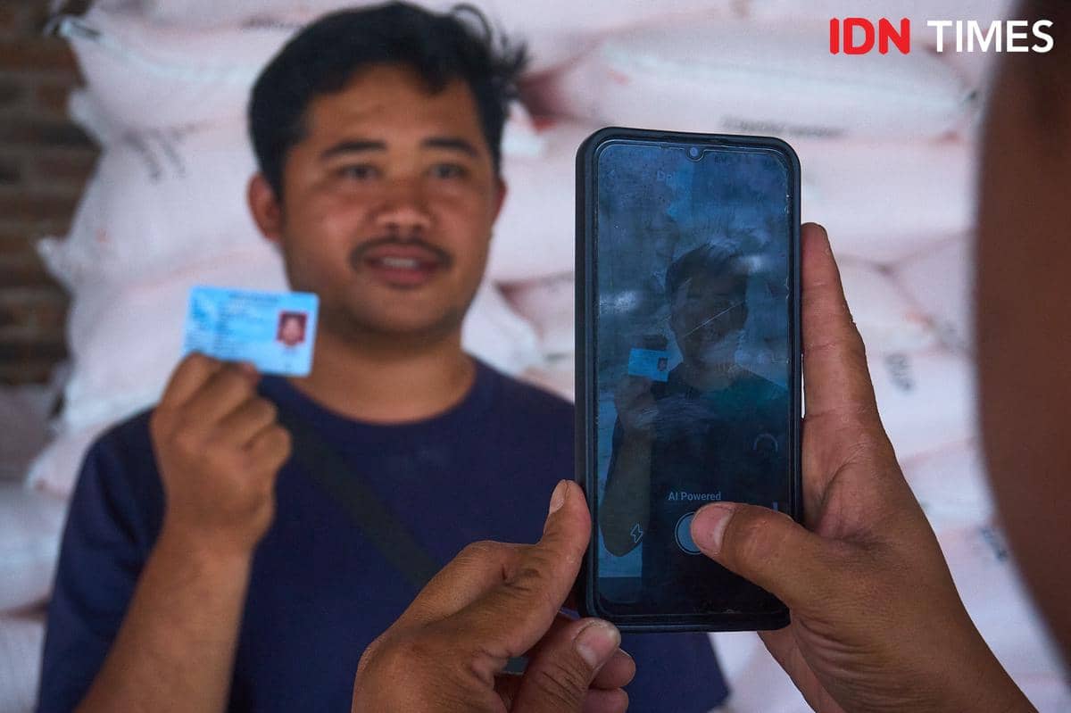 Petugas kios Penerima Pupuk pada Titik Serah (PPTS) UD Jambul, Fakhur Arif memfoto petani Desa Pucang, Secang, Magelang, Juandika yang menebus pupuk bersubsidi menggunakan Kartu Tanda Penduduk (KTP), Senin (22/12/2025). (IDN Times/Dhana Kencana)