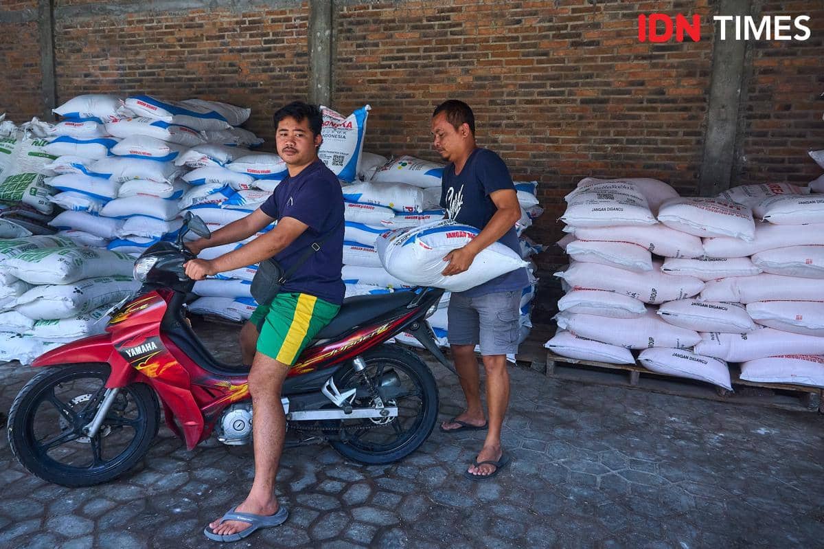 Fatkhur Arif (kanan), petugas kios Penerima Pupuk pada Titik Serah (PPTS) menyerahkan satu karung pupuk NPK Phonska kepada Juandika (kiri) di kios PPTS UD Jambul di Desa Pucang, Secang, Magelang, Senin (22/12/2025). (IDN Times/Dhana Kencana)