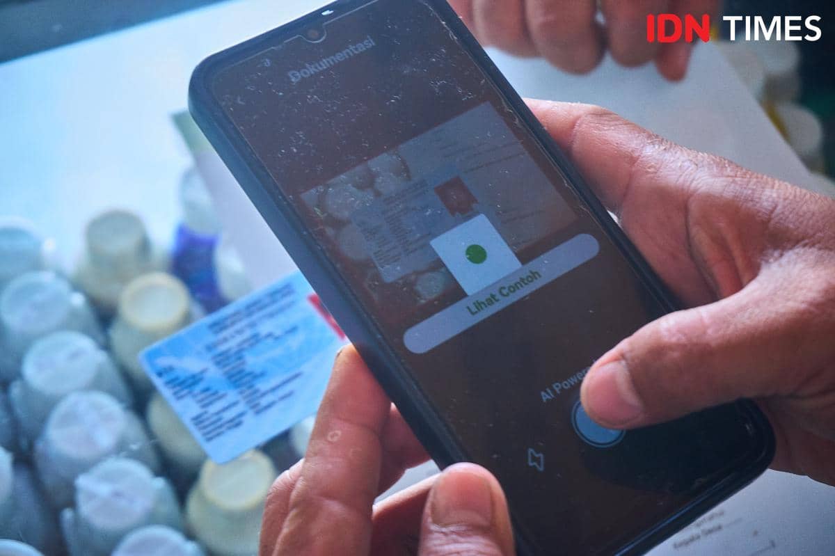 Fatkhur Arif, petugas kios Penerima Pupuk pada Titik Serah (PPTS) memindai Nomor Induk Kependudukan (NIK) Kartu Tanda Penduduk (KTP) menggunakan aplikasi i-Pubers melalui smartphone, dengan layar menampilkan data alokasi pupuk petani, Senin (22/12/2025). Sistem digital tersebut mengintegrasikan data petani dari e-RDKK dengan stok pupuk secara real-time. (IDN Times/Dhana Kencana)