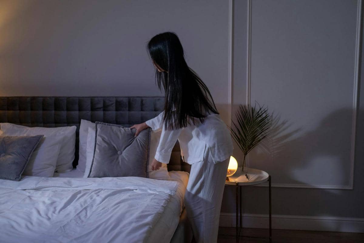 Seorang perempuan merapikan tempat tidur, bersiap untuk tidur.