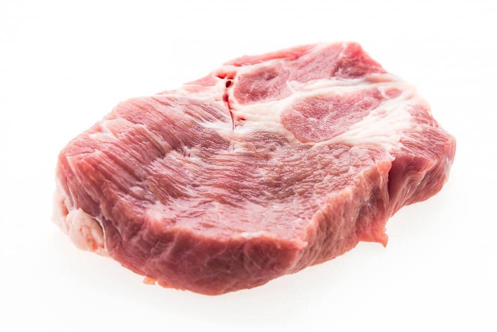 Potongan daging babi mentah berwarna merah muda dengan sedikit lemak putih di atas permukaan meja putih.