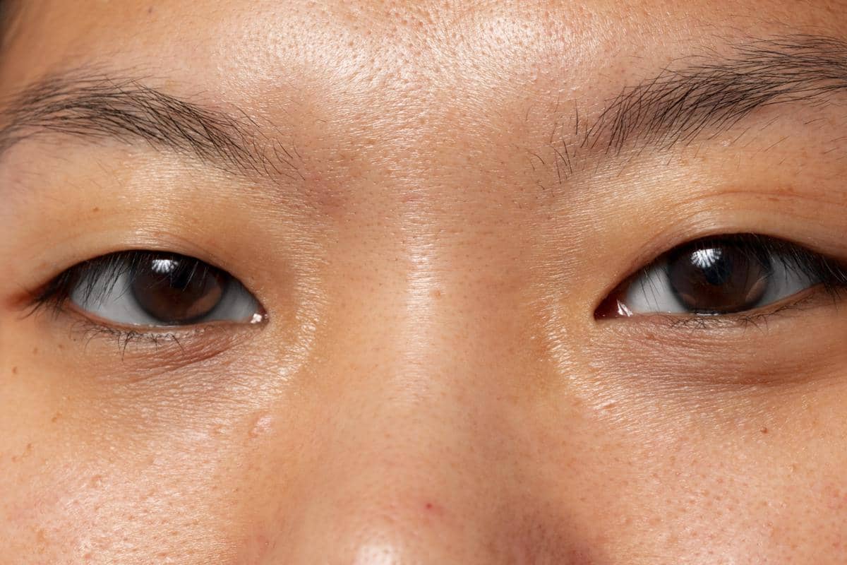 Tampilan close-up sepasang mata seseorang dengan alis alami dan kulit wajah terlihat jelas, menunjukkan detail tekstur kulit di area sekitar mata dan hidung dalam pencahayaan yang merata.