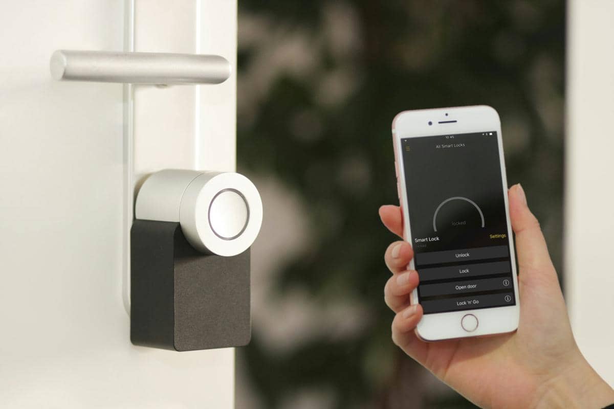 Seseorang mengoperasikan kunci pintu pintar menggunakan aplikasi di ponsel untuk mengunci dan membuka pintu rumah secara digital.