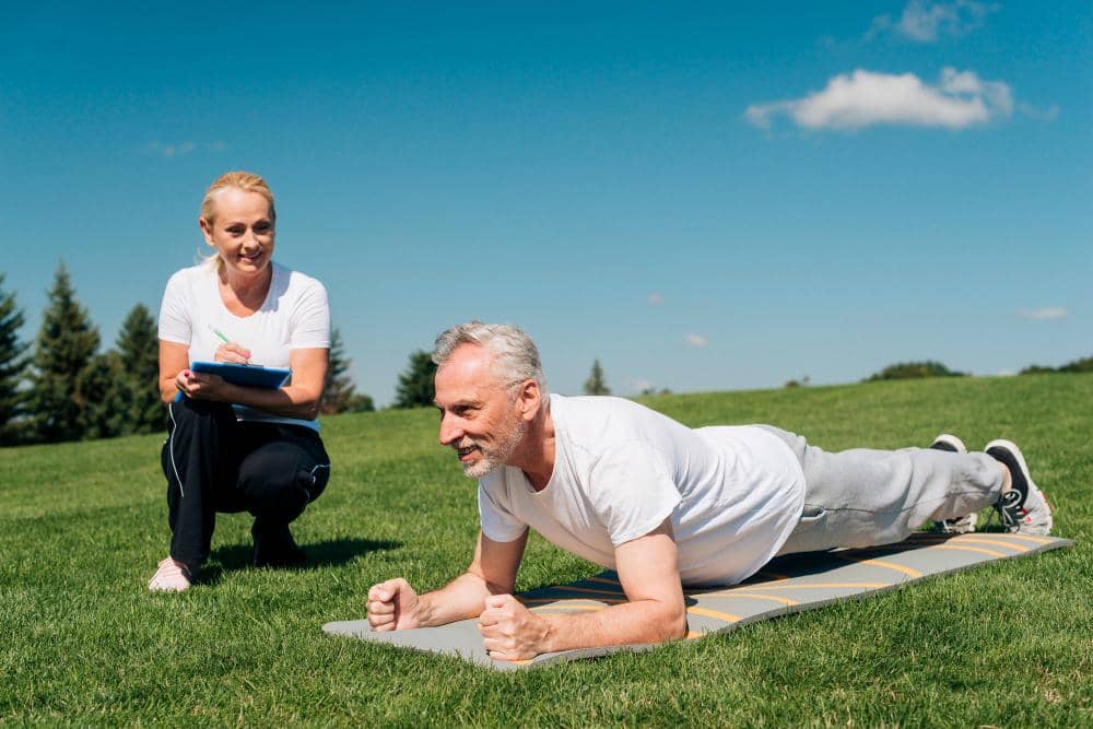 Seorang lansia berlatih plank dipandu oleh pelatih.