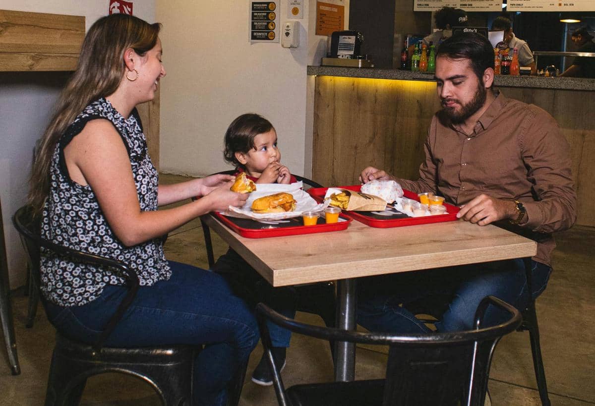 Sebuah keluarga terdiri dari dua orang dewasa dan seorang anak kecil sedang makan bersama di meja restoran dengan suasana hangat.