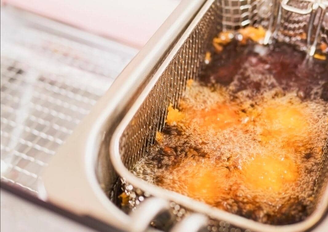 Minyak bekas menggoreng dalam wajan dengan sisa makanan, menggambarkan limbah minyak goreng rumah tangga.