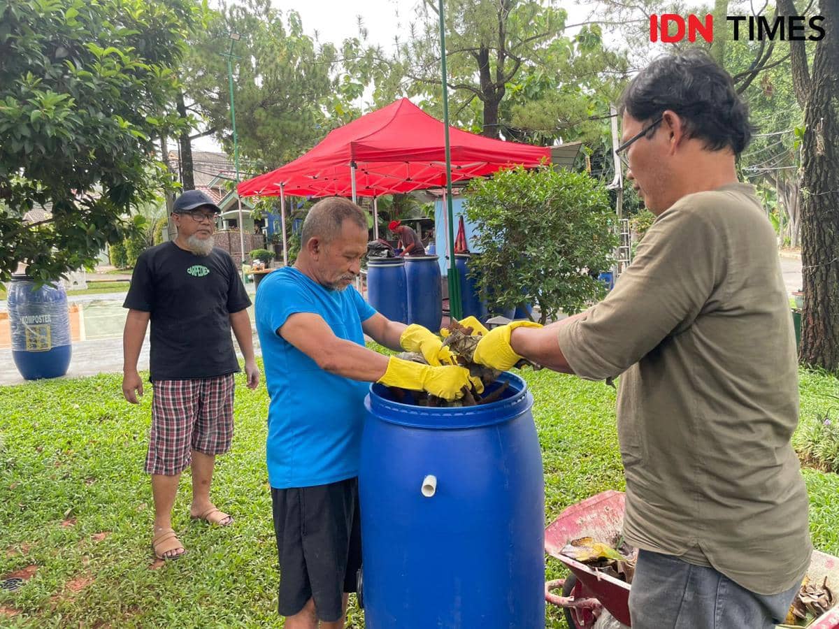 Beberapa warga Ciputat mengenakan sarung tangan kuning sedang mengolah sampah organik ke dalam tong biru untuk dijadikan kompos di area terbuka.