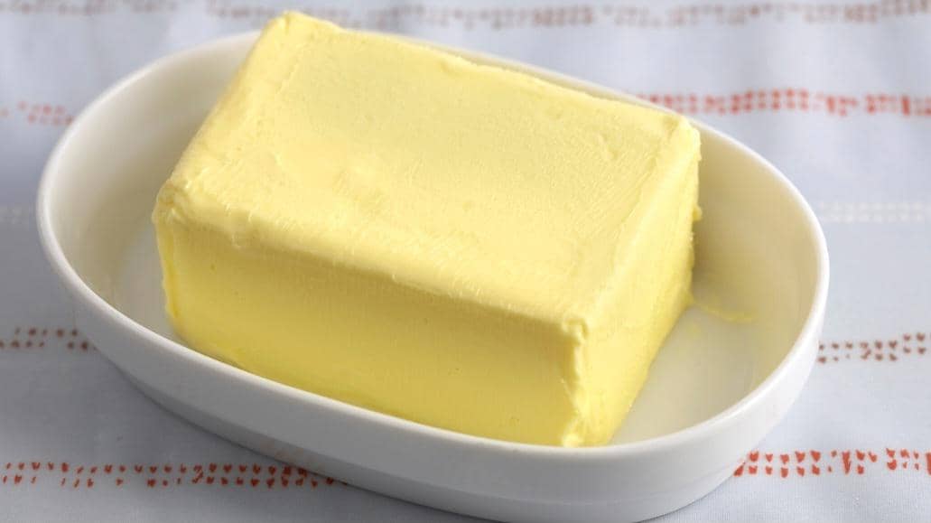 Sekeping mentega berwarna kuning pucat sebagai bahan makanan untuk memasak, memanggang, dan olesan roti.