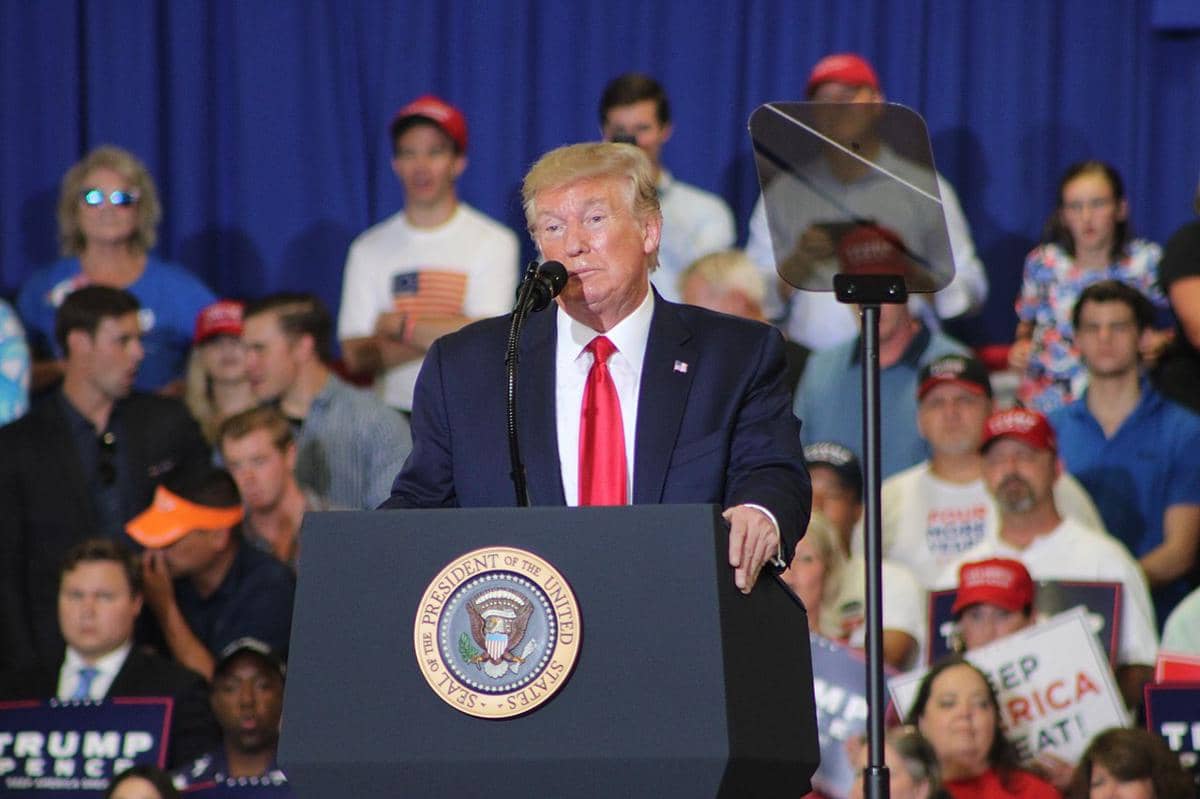 Presiden Amerika Serikat, Donald Trump, sedang berpidato di atas mimbar.