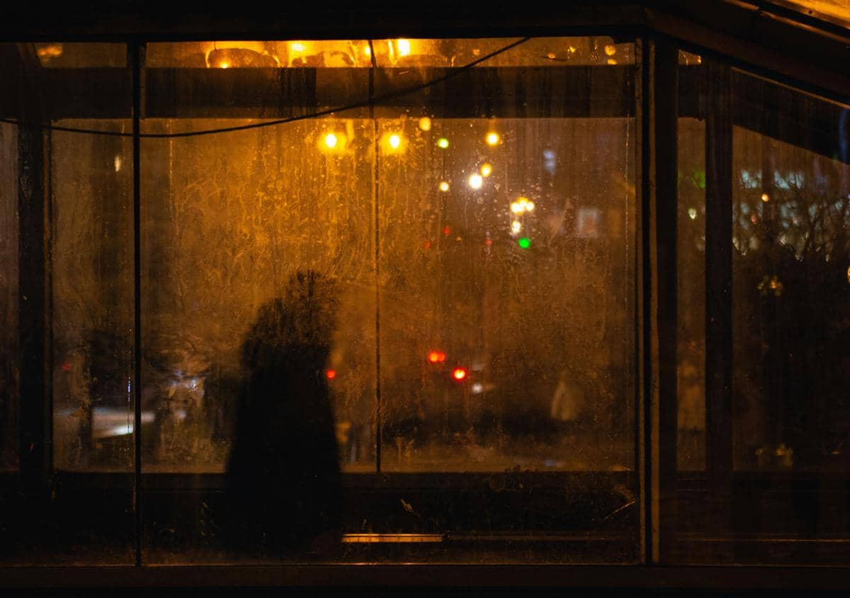 Ilustrasi seseorang berdiri di depan jendela saat hujan dengan suasana rindu.