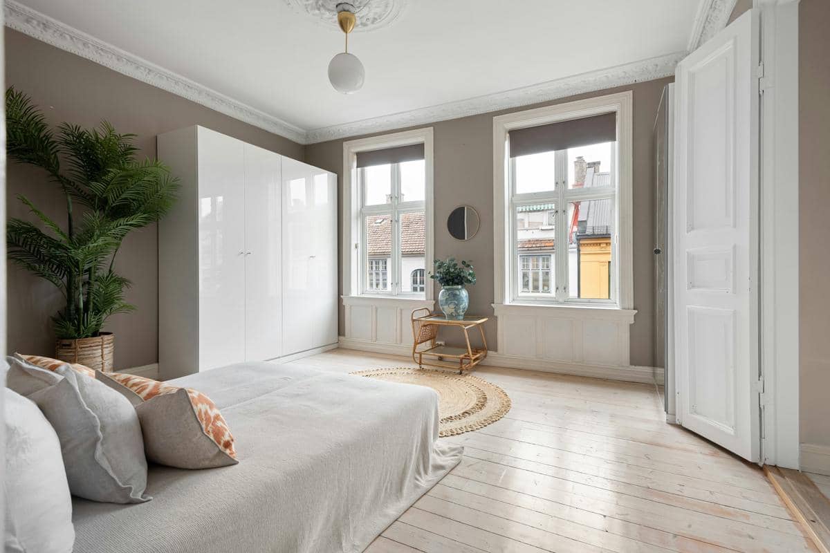 Interior apartemen studio bergaya minimalis modern dengan dinding netral, tempat tidur sederhana, lemari putih, dan tanaman hias di sudut ruangan.