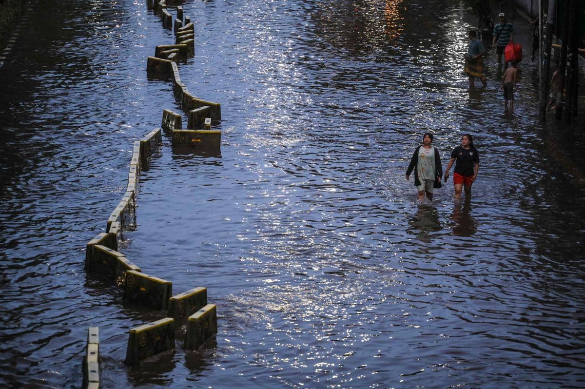 Warga berjalan melintasi genangan air di kawasan Gunung Sahari, Jakarta, Minggu (18/1/2026).